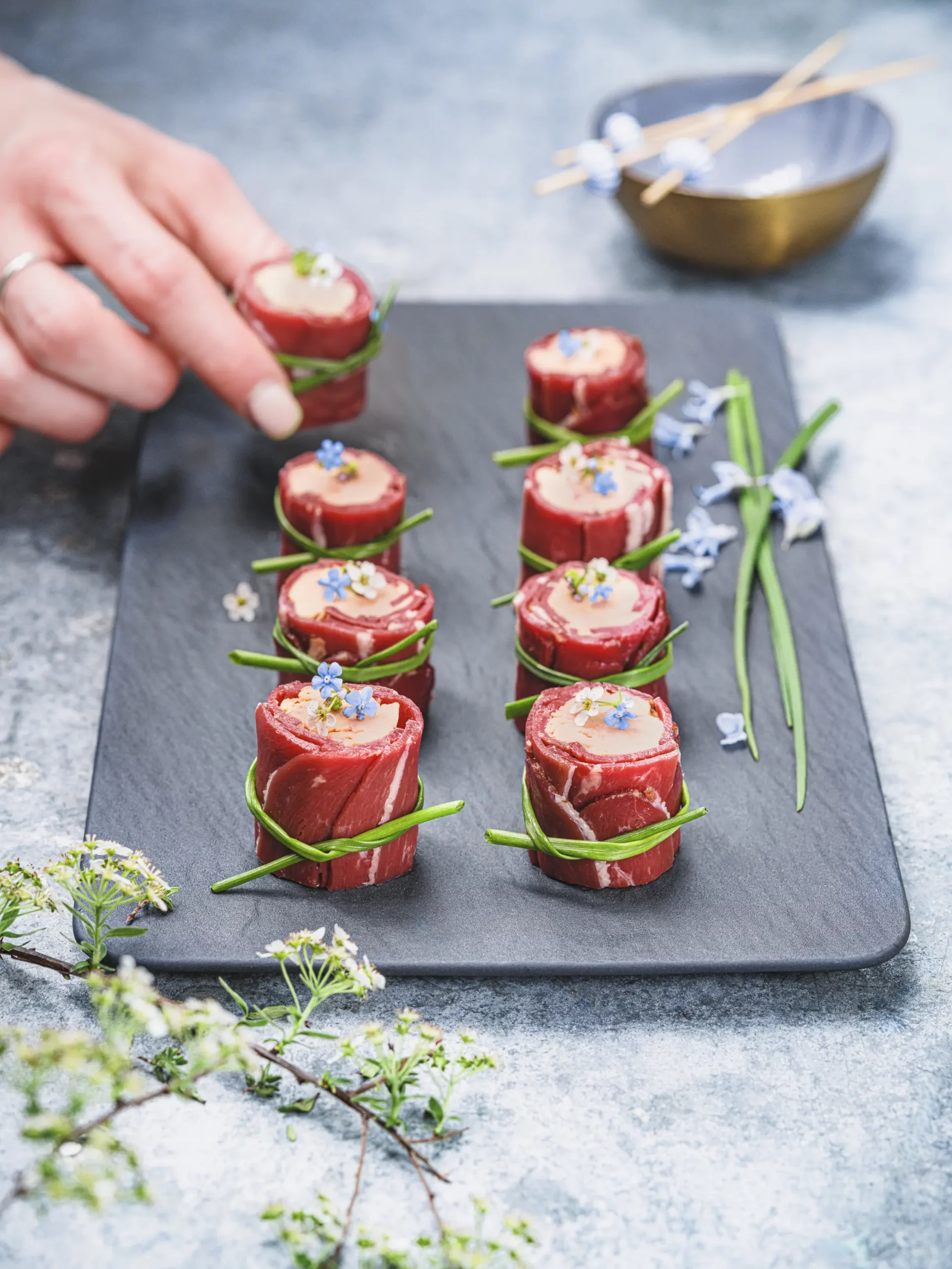 Plateau d’amuse-bouches avec foie gras roulé dans du bœuf, ficelés à la ciboulette, décorés de fleurs